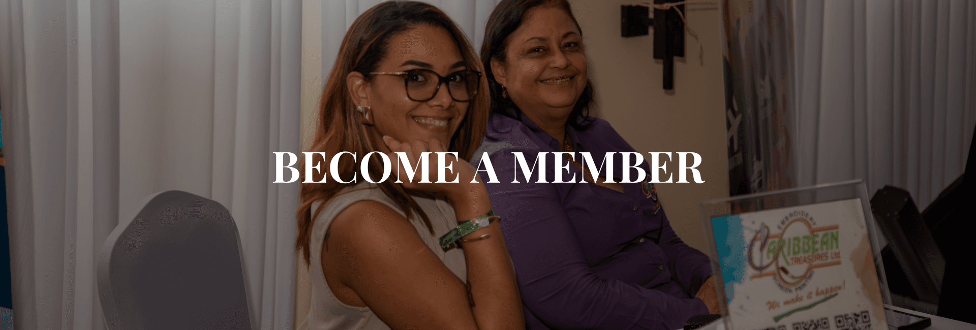 Two women smile at a booth promoting membership.