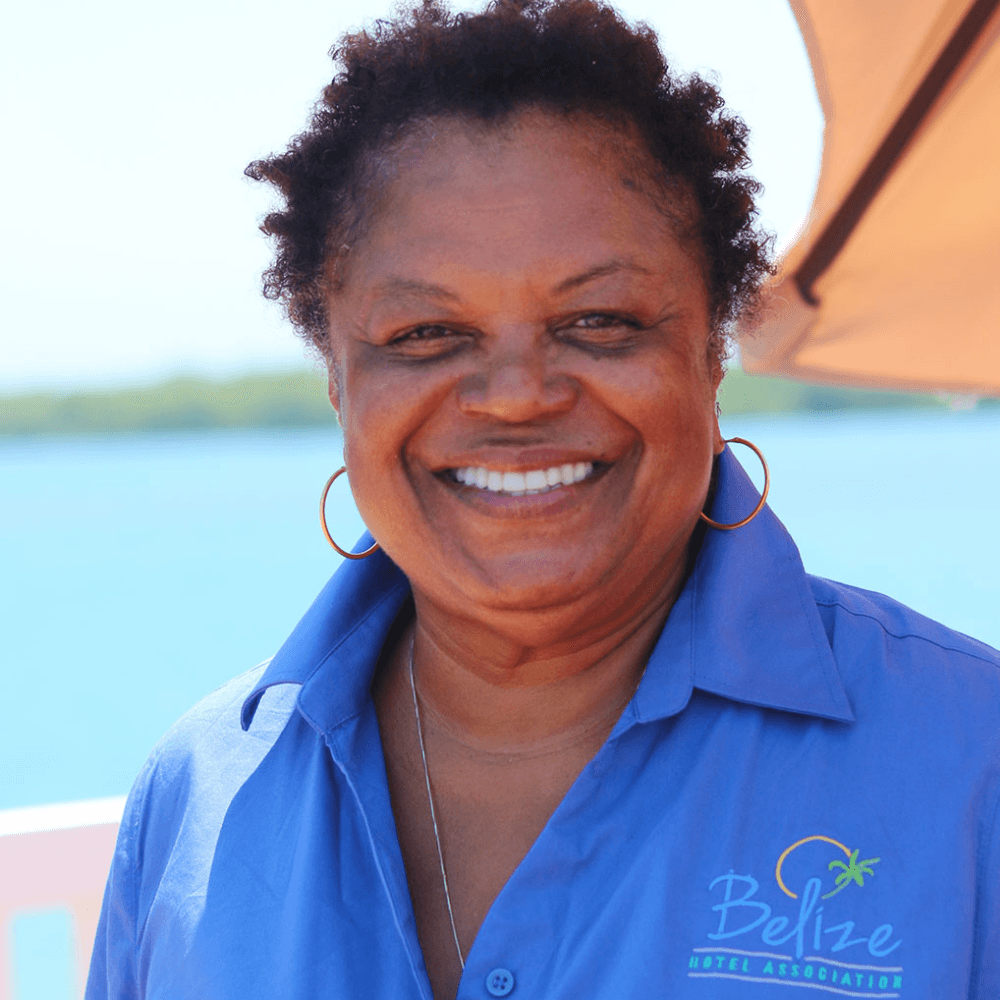 A smiling woman in a blue shirt stands in front of a body of water.