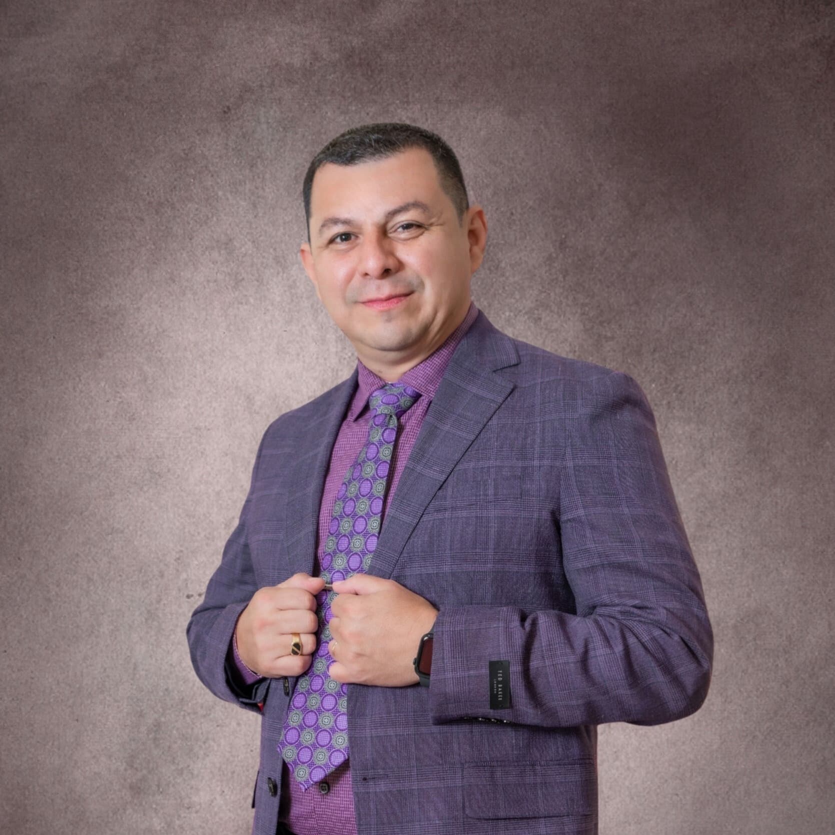 A man in a purple suit and patterned tie poses confidently against a textured background.
