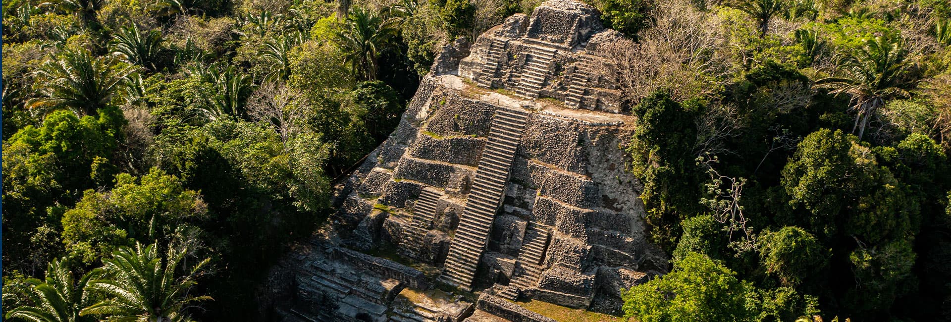 An aerial view of a stepped pyramid surrounded by dense tropical vegetation.