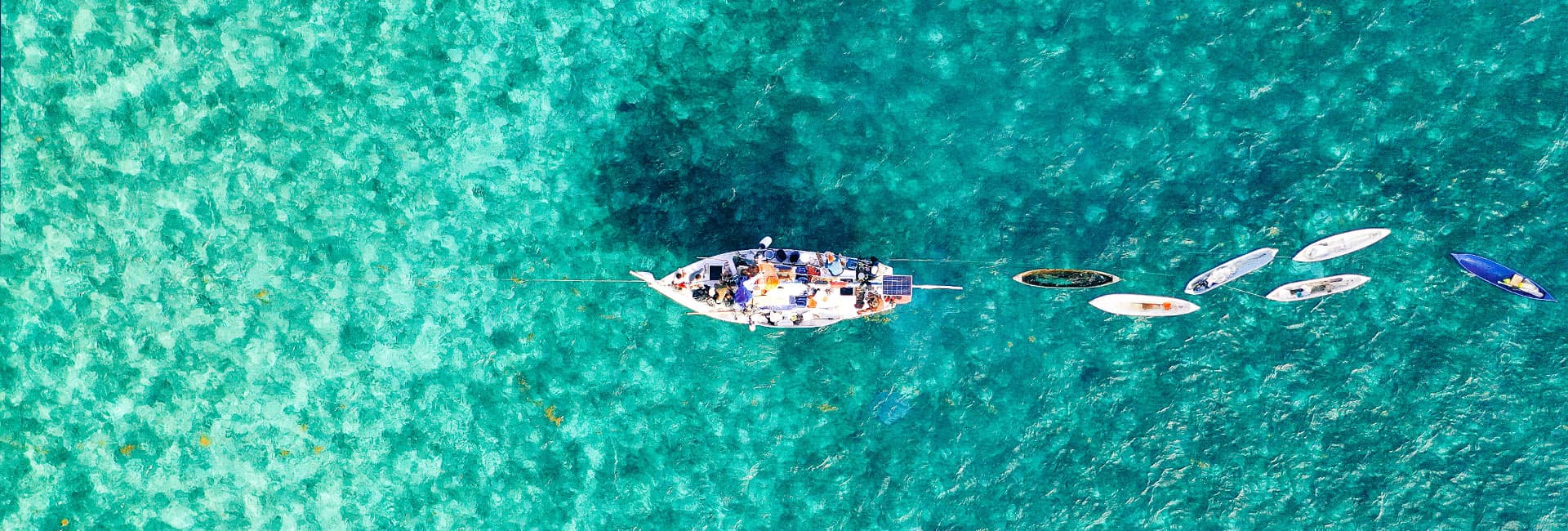 An aerial view of a large boat surrounded by several smaller boats in clear turquoise water.