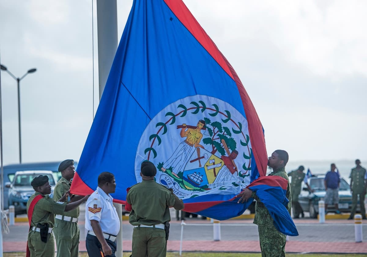 A group of soldiers and officials are raising the flag of Belize during a ceremony.
