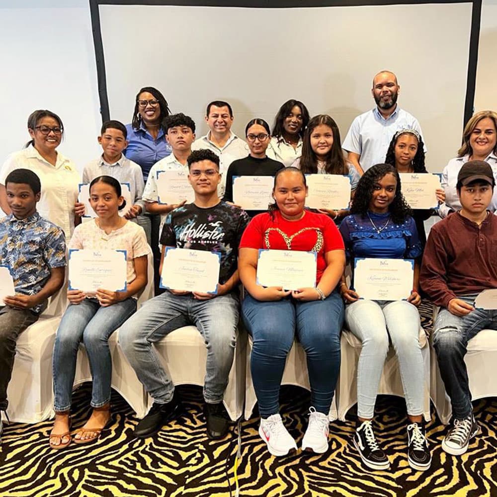 A group of teenagers and adults proudly hold certificates in a celebratory setting.
